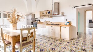 A modern kitchen with white cabinetry, a gas stove, and a dining area with a wooden table and chairs. - Exclusive apartment in villa facing the sea_Baia di Punta Prosciutto (Torre Lapillo)
