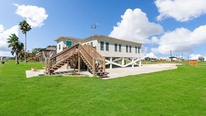 A beachfront property with a wooden staircase leading to a white building, a grassy lawn, and palm trees. - Home on Caney Creek with Pier & RV spot (Sargent)