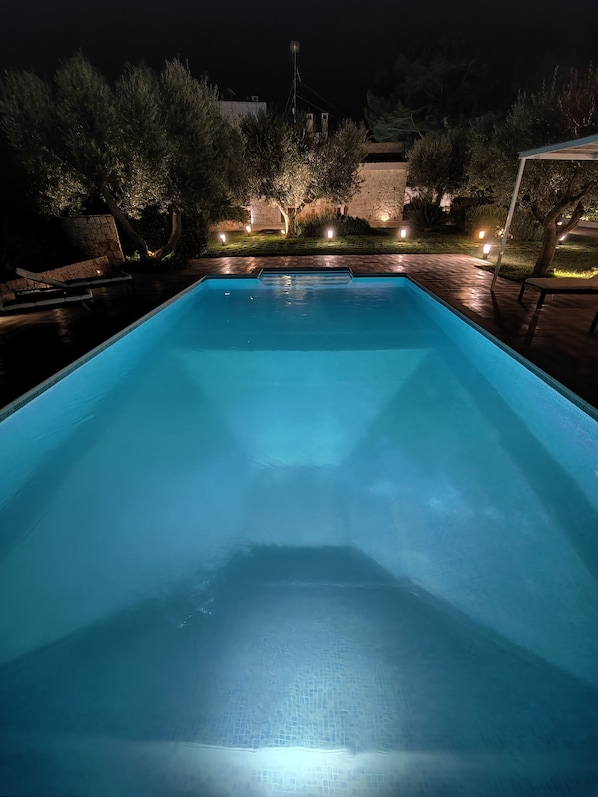 Une piscine rectangulaire à l’eau d’un bleu limpide, entourée d’un mur de pierre et éclairée par un système d’éclairage d’ambiance.