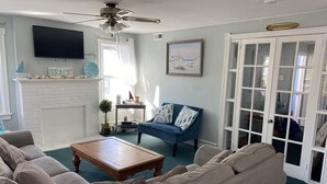 A living room with a fireplace, a ceiling fan, a blue sofa, and a large window.