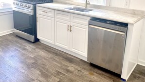 A modern kitchen with white cabinetry, a stainless steel dishwasher, a built-in oven, and a microwave.