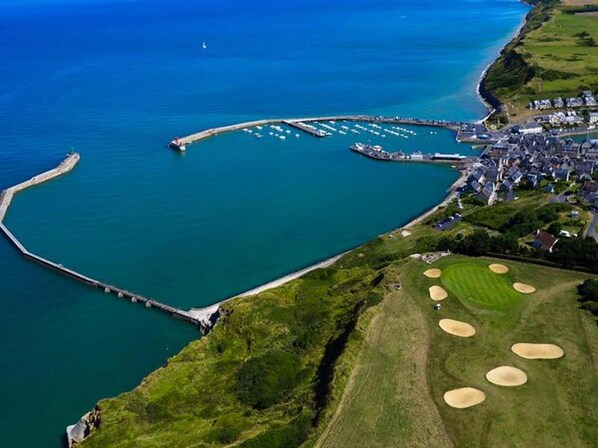 An aerial view of a coastal area with a marina, residential buildings, and a golf course.
