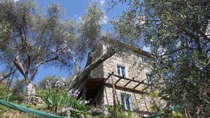 Una casa in pietra con un balcone in legno, immersa tra alberi e vegetazione.