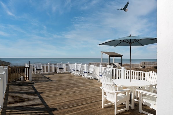 Um deck de madeira com cadeiras brancas e uma mesa, com vista para o oceano.
