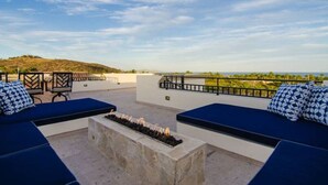 Una terrazza sul tetto con sedute imbottite blu, un elemento decorativo a fuoco e vista su una collina in lontananza.