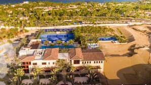 Vista aerea di un resort con diverse piscine, proprietà sulla spiaggia e vegetazione lussureggiante.