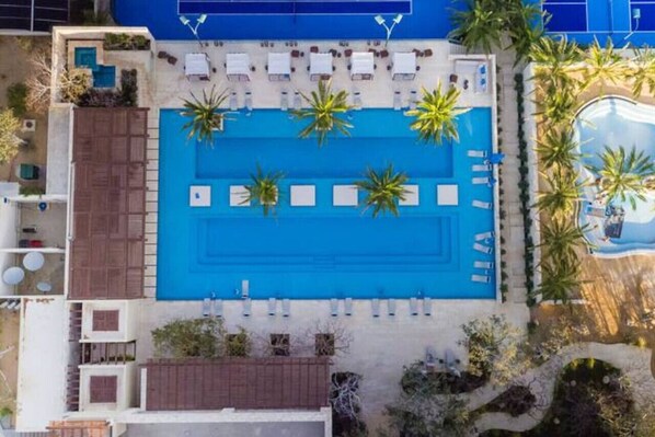 An aerial view of a hotel with a large blue pool surrounded by palm trees and sun loungers. - Palmilla Dunes 521 Casa Cobra 3BR w/Lux Golf Cart (Palmilla)