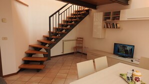 A modern kitchen with a wooden staircase, a dining area with a table and chairs, and a television on a stand. - Large duplex apartment sleeps 5, private parking space, in the center  (Ravenna)