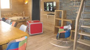 A cozy room with a wooden floor, a red suitcase, a rocking chair, a wooden table, and a television mounted on the wall. - Exeptional luxury duplex of 85 m² in Val Thorens for 8 people (Les Belleville)