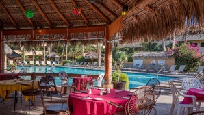 Un espace aménagé au bord de la piscine, comprenant un coin salon couvert, des chaises longues et une table à manger pour deux personnes.