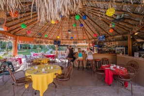 An outdoor restaurant with thatched roofs, wicker furniture, and a bar area.