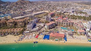 Vue aérienne d’une station balnéaire comprenant plusieurs bâtiments d’hôtel, une plage avec des parasols et une piscine.