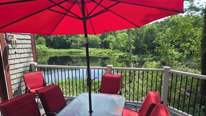 Een terras met tafel en stoelen, een rode parasol en uitzicht op een meer.