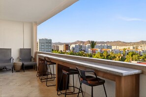 A balcony with a bar area, seating, and a view of buildings and mountains.