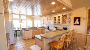 A kitchen with wooden cabinets, a central island with bar stools, a microwave, and a sink. - 6 bedrooms, elevator,  3 minute walk to the beach. (Kill Devil Hills)