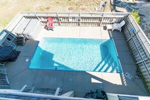 Et rektangulært pool med træterrasse, omgivet af et træhegn og et par liggestole.