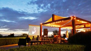 An outdoor movie screening area with a large screen, seating, and string lights.