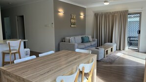 A modern living room with a wooden dining table, white chairs, a grey sofa, and a small ottoman. - Seadaze 1 - Rainbow Beach. Gorgeous unit close to the beach. Aircon. Pool. Wifi (RAINBOW BEACH)