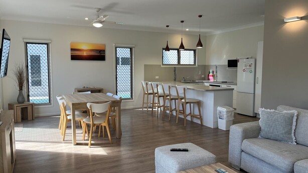 A modern kitchen with a central island, a dining area with wooden chairs, and a grey sofa in a living area. - Seadaze 1 - Rainbow Beach. Gorgeous unit close to the beach. Aircon. Pool. Wifi (RAINBOW BEACH)