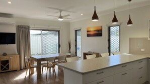 A modern kitchen with a central island, dining area with chairs, a ceiling fan, pendant lights, and a TV mounted on the wall. - Seadaze 1 - Rainbow Beach. Gorgeous unit close to the beach. Aircon. Pool. Wifi (RAINBOW BEACH)