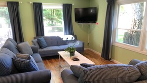 A living room with a grey sofa, striped couches, a flat-screen TV, and a wooden coffee table. - ☀️Summer dates available!  (Mears)