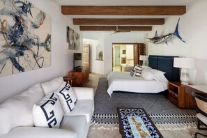 A modern hotel room with a large abstract painting, a ceiling fan, a bed with a dark headboard, a white sofa with patterned cushions, and a patterned rug. - Luxury Oceanfront Villa - Endless Panoramic Ocean and Pool Views! (Cabo San Lucas)
