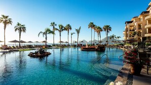 A clear blue pool with lounge chairs and palm trees, surrounded by a resort building. - Luxury Oceanfront Villa - Endless Panoramic Ocean and Pool Views! (Cabo San Lucas)