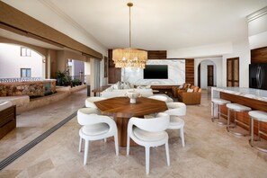 A spacious living area with a large wooden dining table surrounded by white chairs, a modern chandelier, and a large flat-screen TV mounted on a marble wall. - Luxury Oceanfront Villa - Endless Panoramic Ocean and Pool Views! (Cabo San Lucas)
