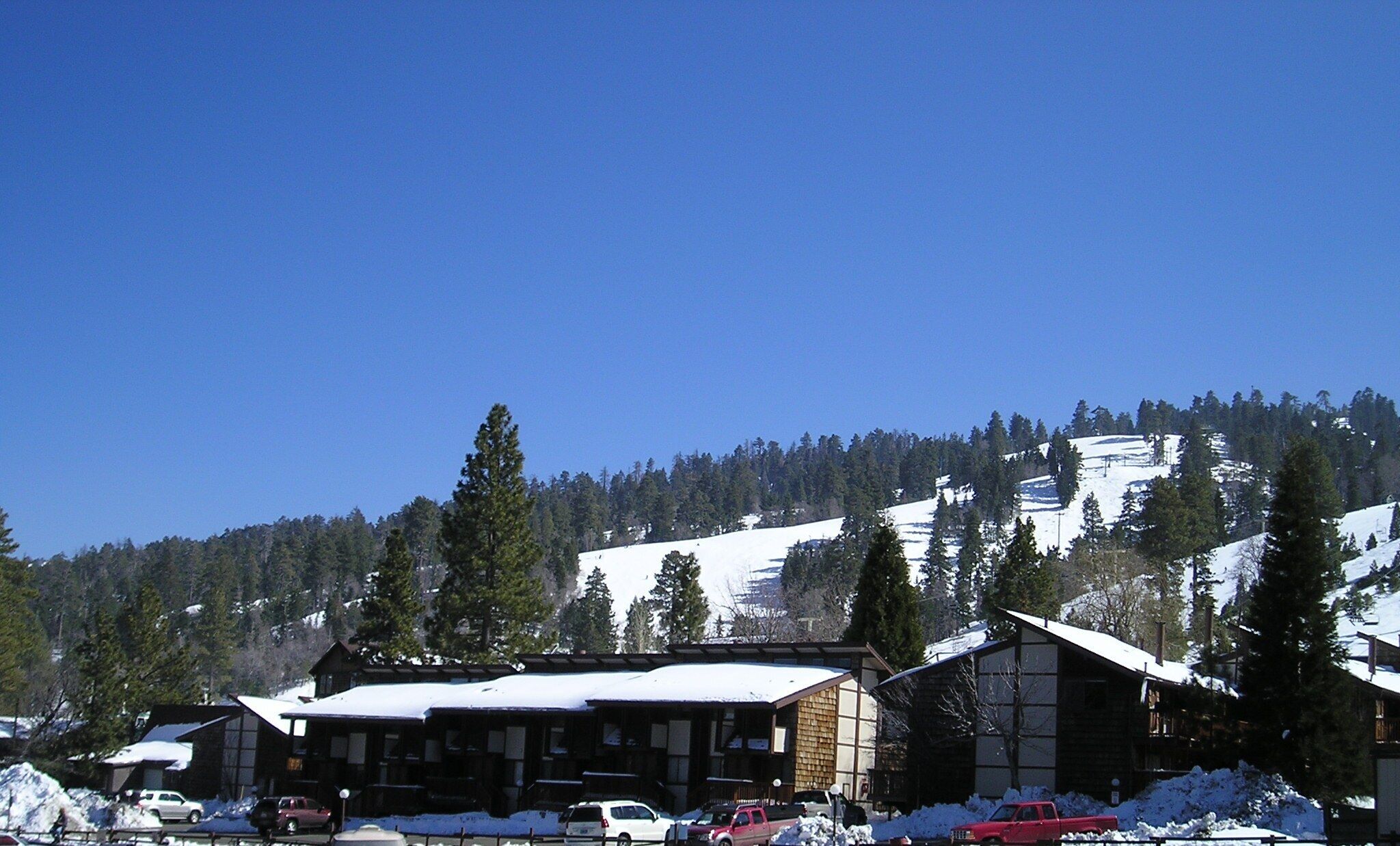 Un chalet de montagne avec un toit enneigé, une façade en bois et une vue sur une montagne couverte de neige.