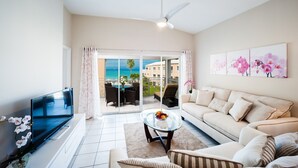 A living room with a TV, sofa, coffee table, and artwork. - Regal Beach Club #231 (Seven Mile Beach)