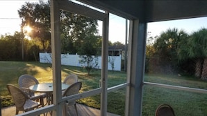 Un patio couvert avec une table et des chaises, donnant sur une pelouse verdoyante, et une clôture blanche en arrière-plan.