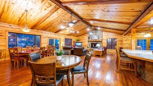 A log cabin interior with a dining area, seating, a fireplace, and a stone wall.