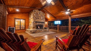 A log cabin with a stone fireplace, wooden deck, and outdoor seating.