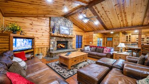 A cozy log cabin interior with a stone fireplace, leather furniture, and a television.