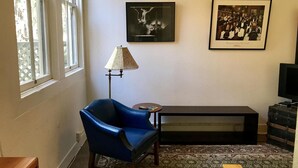 Een kamer met een blauwe fauteuil, een lamp, een lijst met een foto, een televisie en een kamerbreed tapijt.