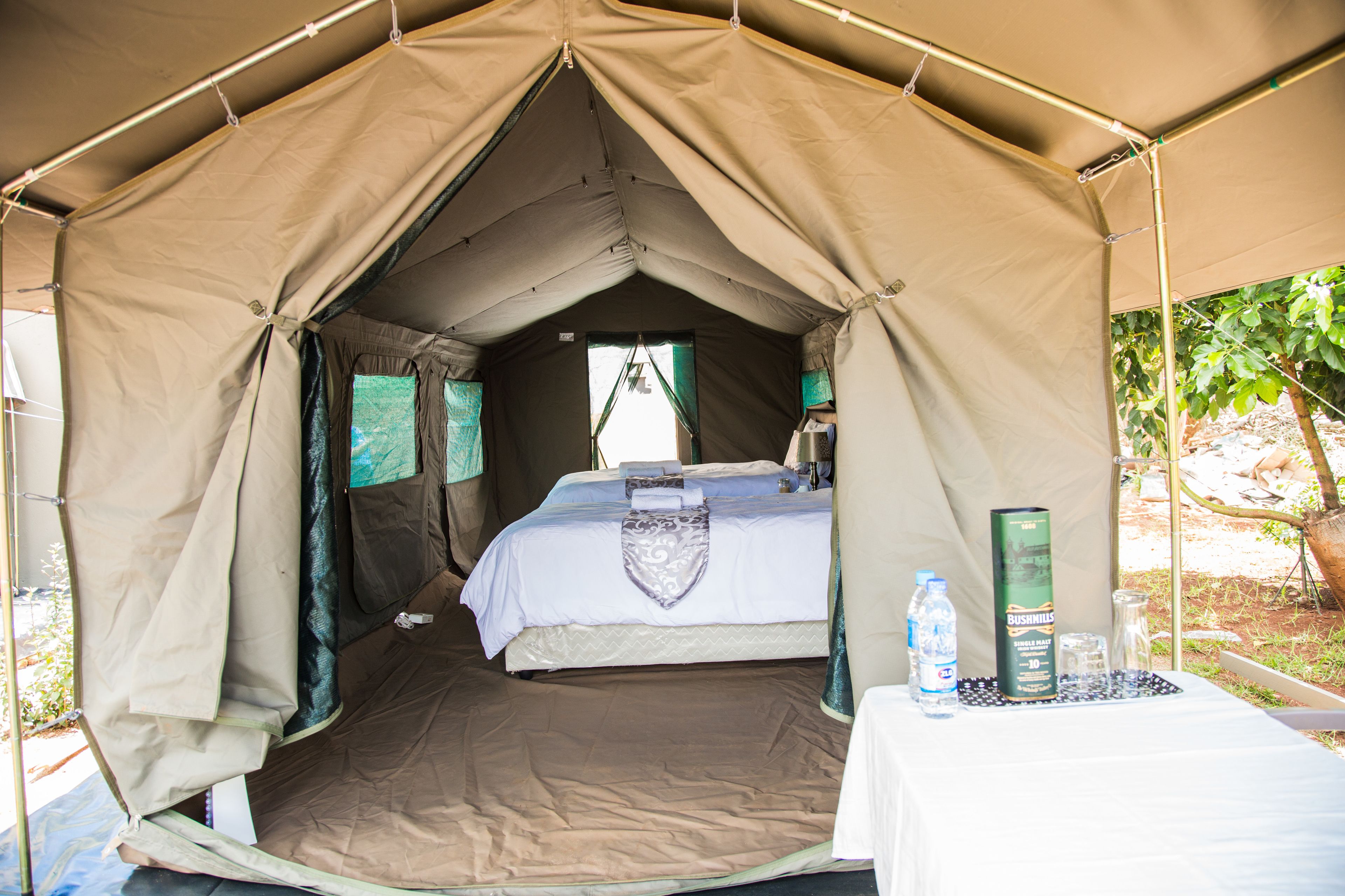 A tent with a bed, a table with a water bottle, and a container.