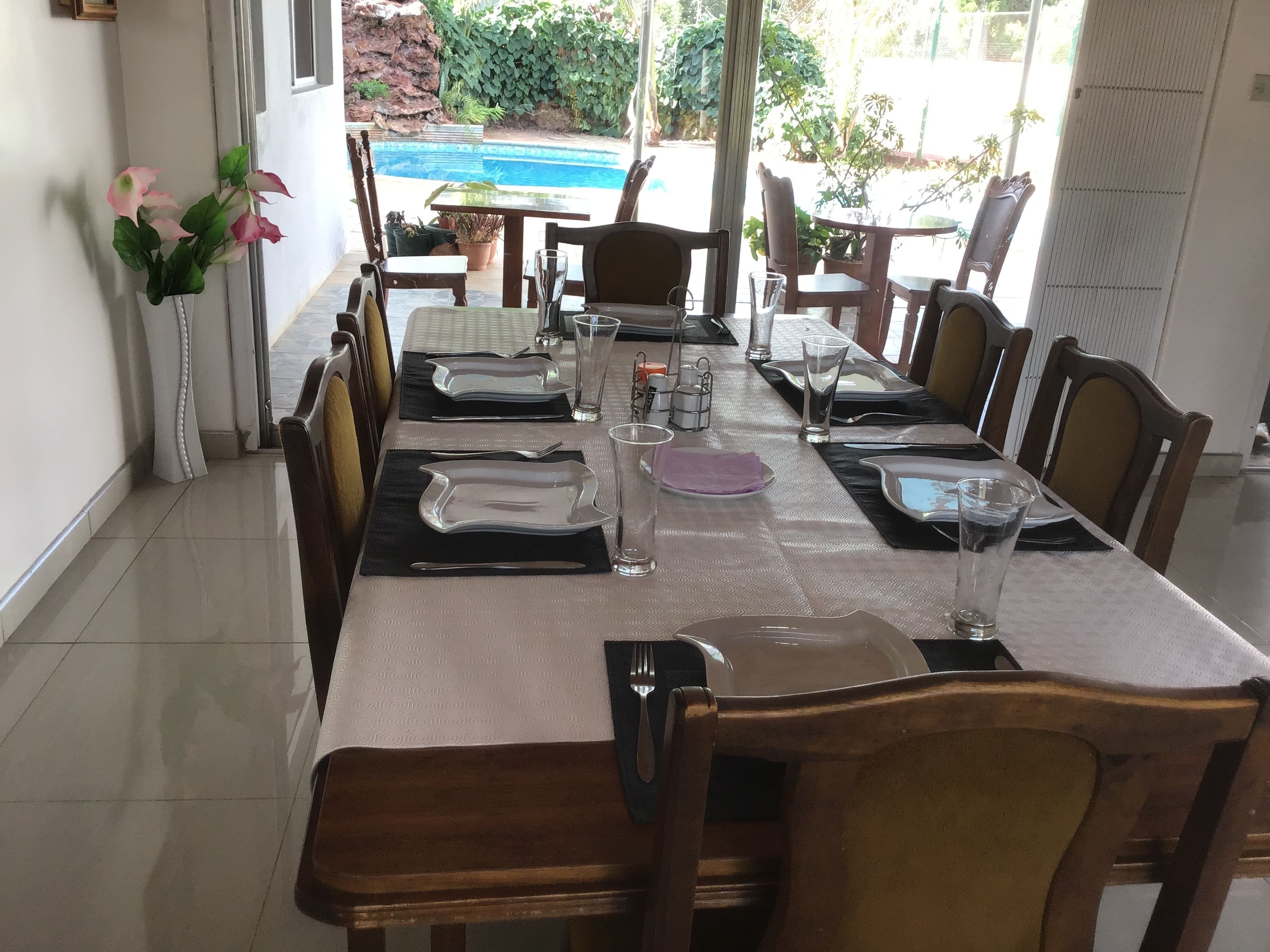 Mesa de comedor preparada para seis personas, con sillas, un florero y vista a una piscina.