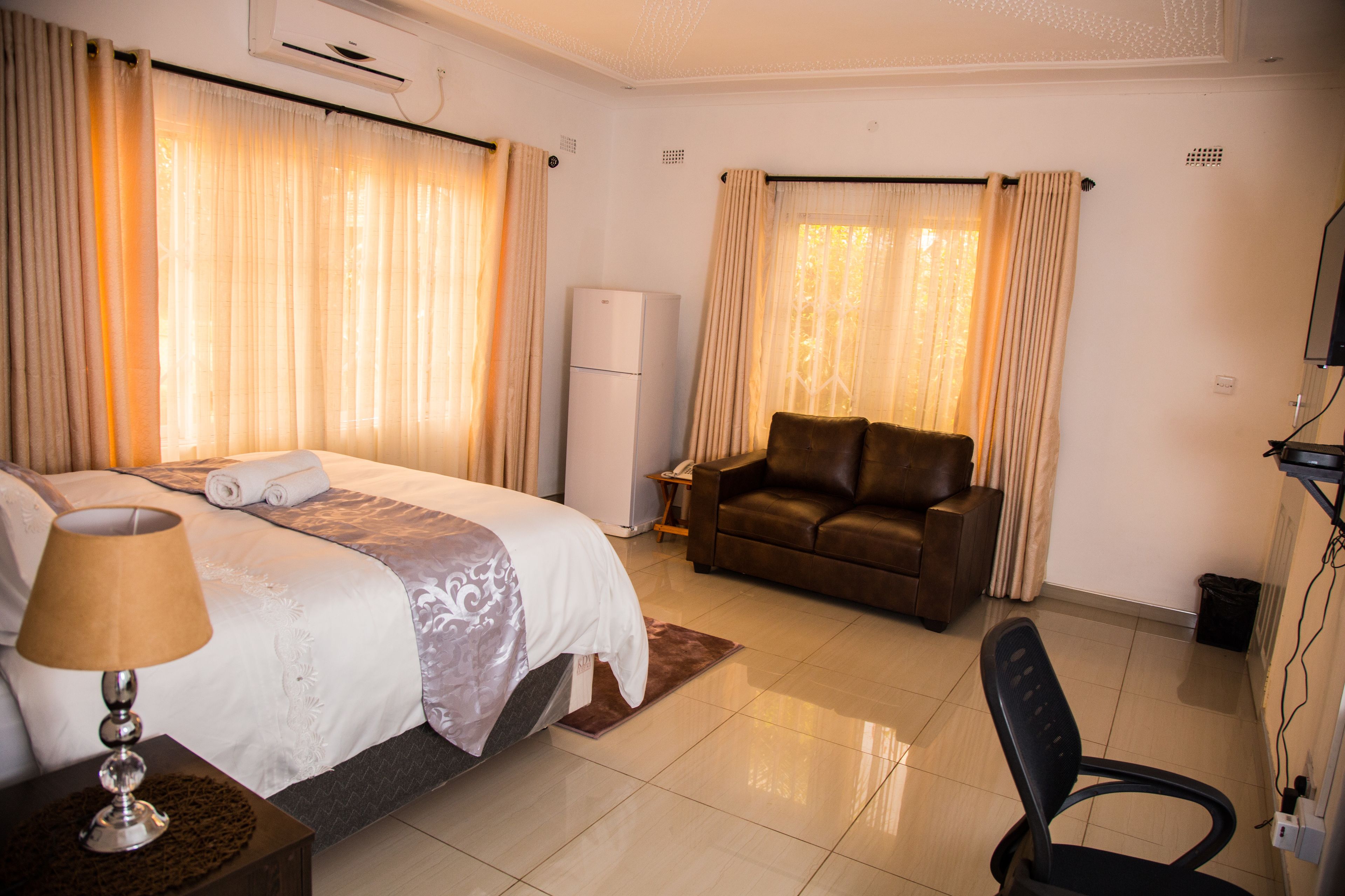 Une chambre d’hôtel avec un lit, un bureau, une chaise, une lampe et des rideaux.