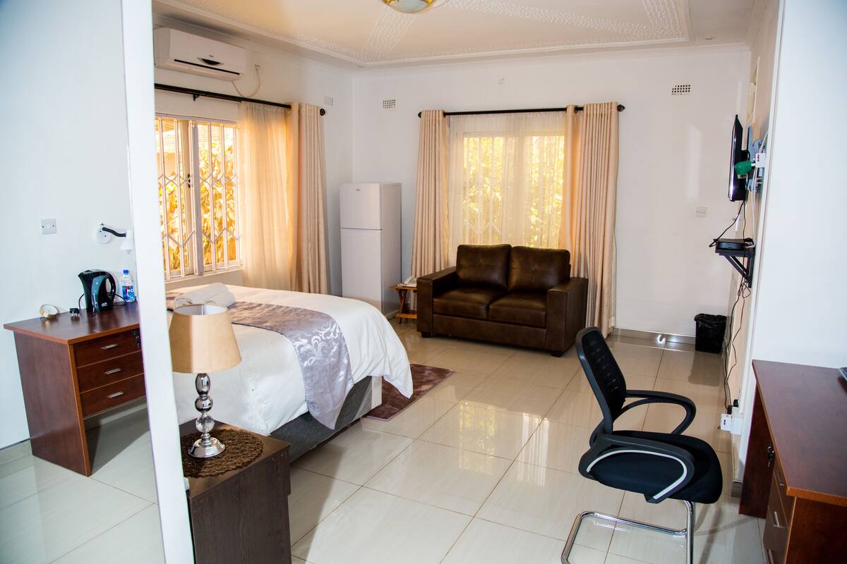 A hotel room with a bed, a desk, a chair, a sofa, and a television.