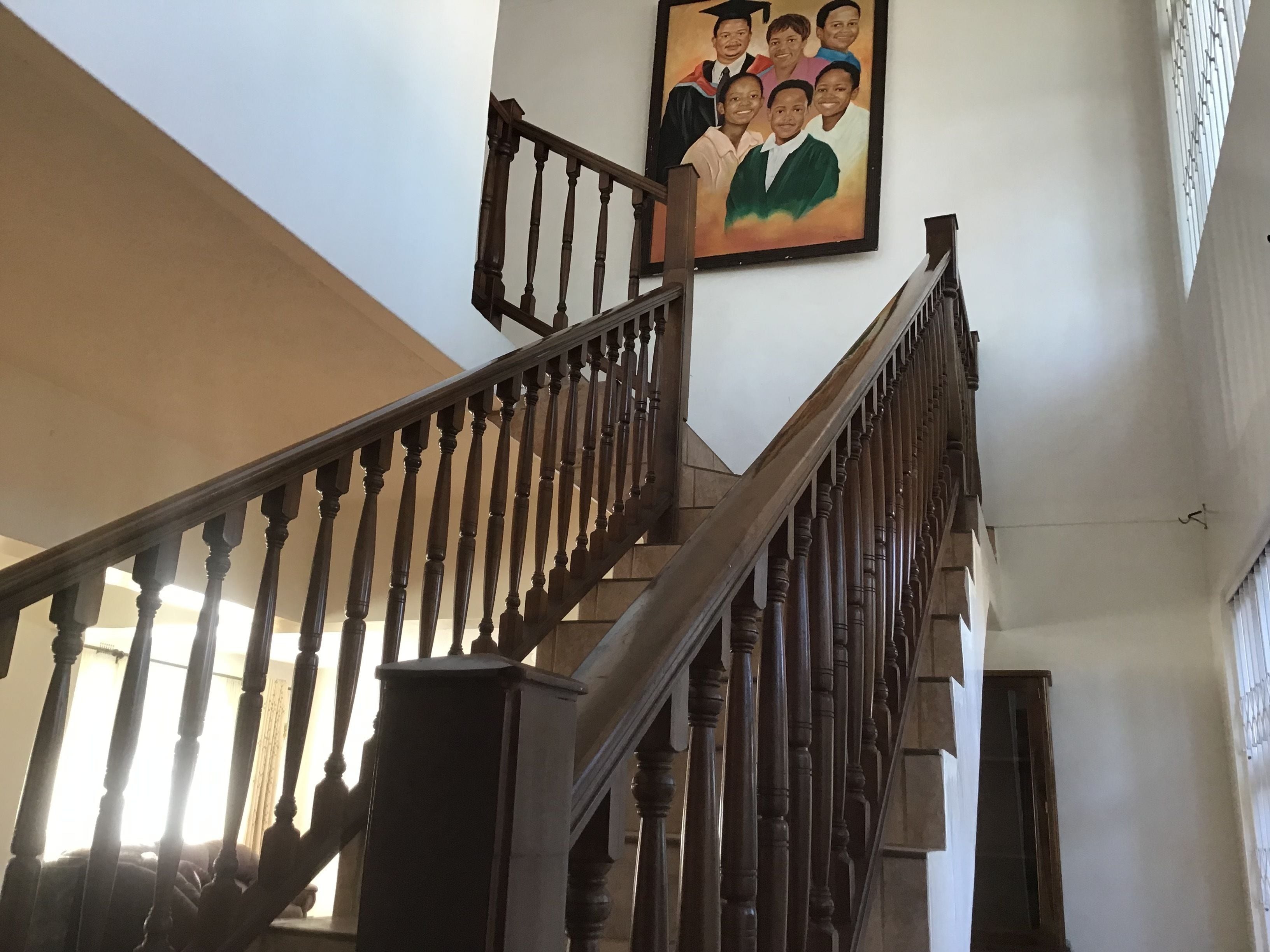 Una escalera de madera con barandilla que lleva a un rellano donde cuelga un retrato enmarcado.