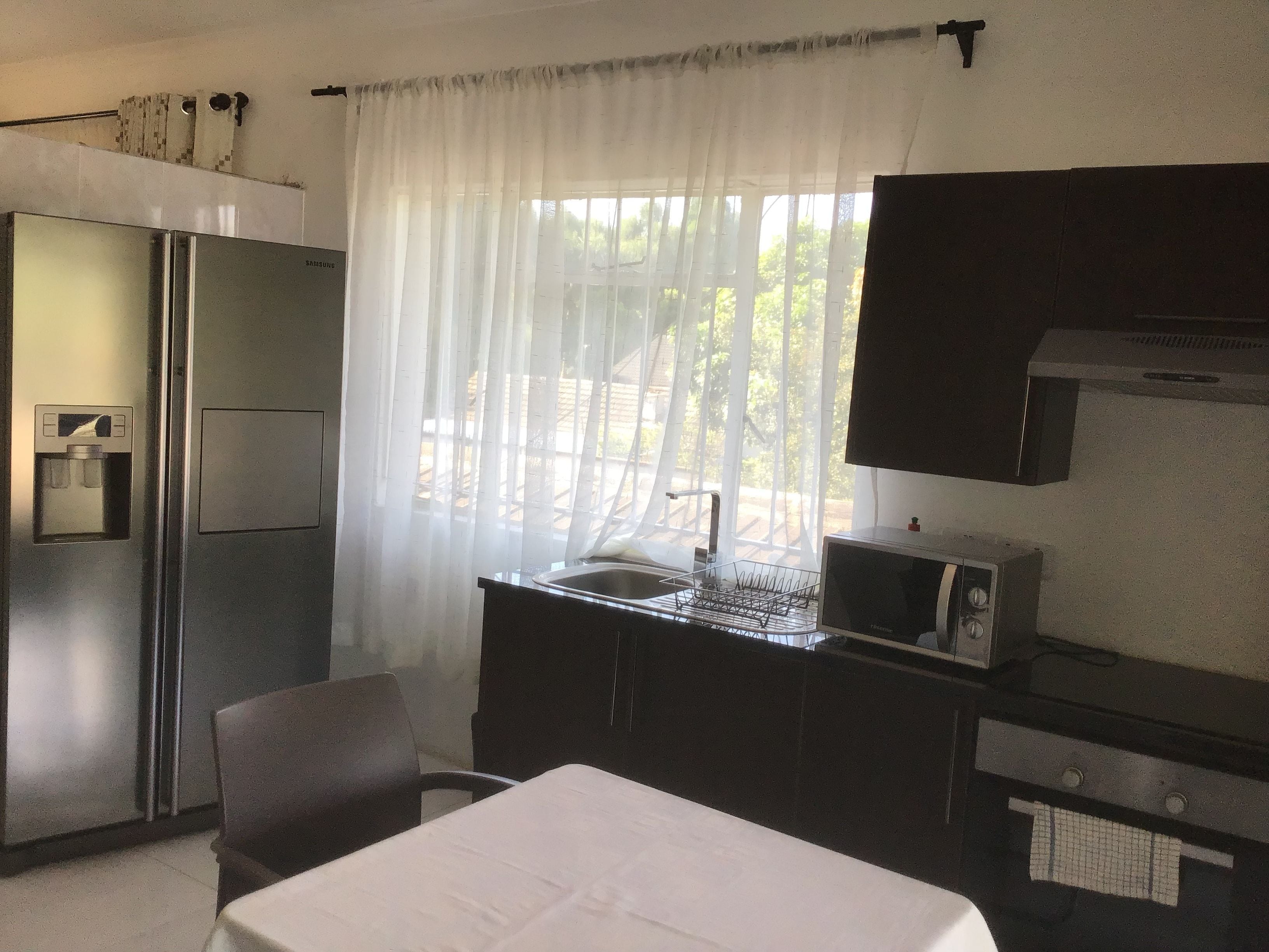 Une chambre d’hôtel compacte comprenant un lit, un bureau avec un micro-ondes, un réfrigérateur et une fenêtre avec des rideaux légers.