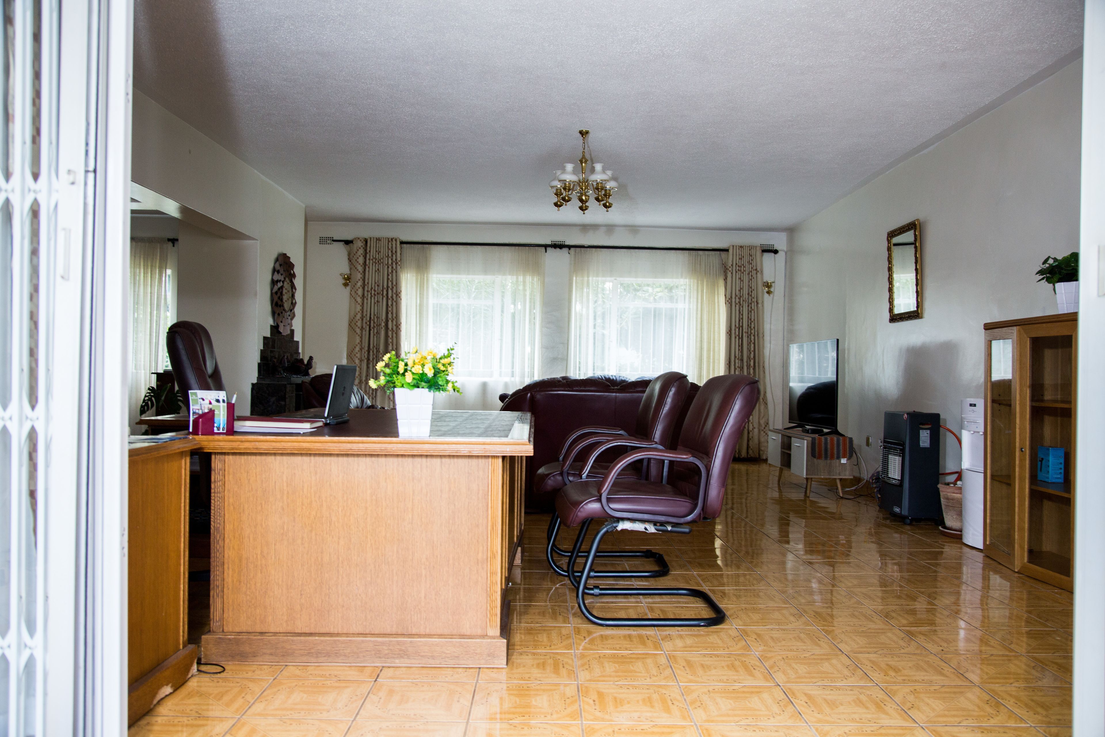 A living room with a wooden desk, a laptop, a potted plant, a chandelier, and a television.