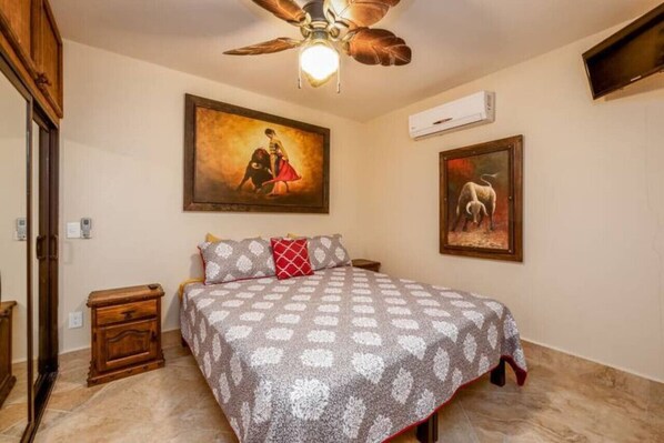 A bedroom with a bed, a ceiling fan, a painting on the wall, and a nightstand.