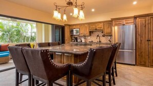 A spacious kitchen with a central island, wooden cabinets, stainless steel appliances, and a chandelier.