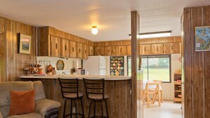 A compact kitchen with wooden cabinets, a refrigerator, a microwave, and a dining area with a table and chairs. - Private Beach Access Trail And Peaceful Wooded Setting (Port Angeles)