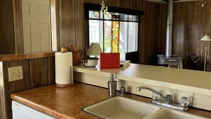 A kitchen with wooden cabinets, a double sink, a dishwasher, and a window with a view. - Private Beach Access Trail And Peaceful Wooded Setting (Port Angeles)