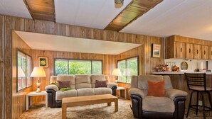A cozy living room with a sofa, armchair, and bench, wooden walls, and large windows. - Private Beach Access Trail And Peaceful Wooded Setting (Port Angeles)