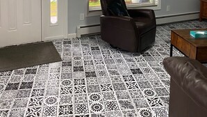 Ein Wohnzimmer mit gemustertem Boden, einem braunen Ledersessel, einem Holztisch und einem an der Wand montierten Fernseher.