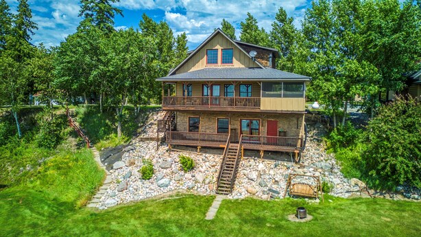 A two-story house with a stone foundation, a wooden deck, and a stone staircase leading to the entrance.