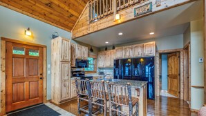 A rustic kitchen with wooden cabinets, a central island with chairs, a microwave, and a refrigerator.